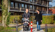 Vrouw en man met kinderwagen lopen voor appartementen langs