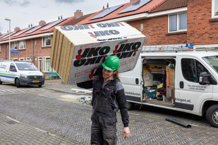 Bouwvakker loopt met isolatiemateriaal naar een huis