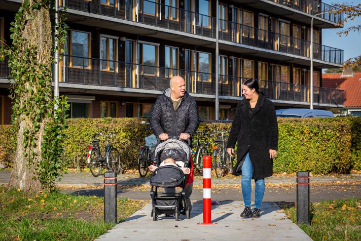 Vrouw en man met kinderwagen lopen voor appartementen langs