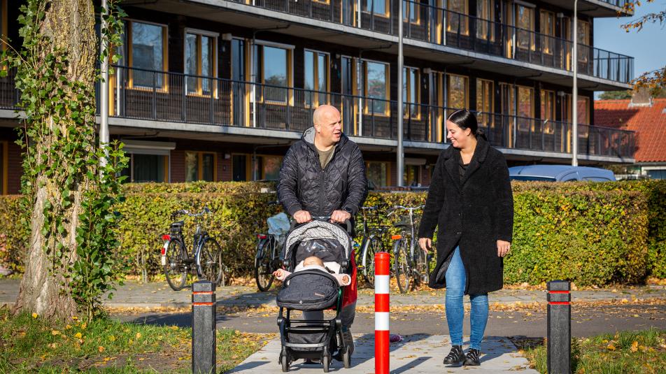 Vrouw en man met kinderwagen lopen voor appartementen langs